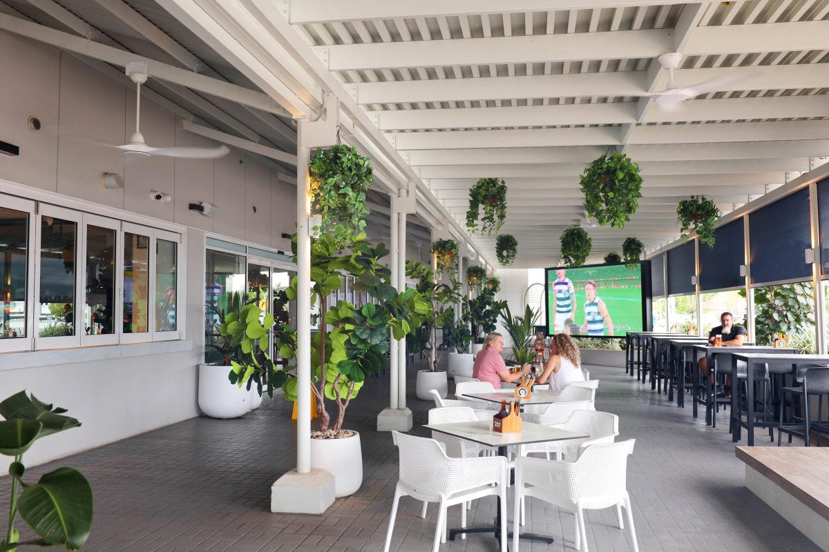 Modern outdoor beer garden at Twin City Hotel with hanging greenery, dining tables. Live and Loud sports screen.